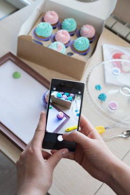 bir kutu kekler ve ahşap bir çerçeve ile bir telefon kadınların elleri tarafından fotoğraf çekimi