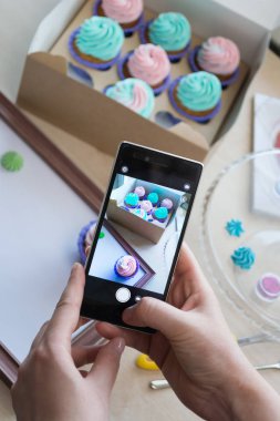 bir kutu kekler ve ahşap bir çerçeve ile bir telefon kadınların elleri tarafından fotoğraf çekimi