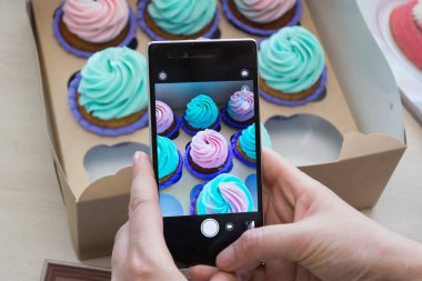 Kadınların elleri tarafından bir kutu bir telefon ile cupcakes ile fotoğraf çekimi