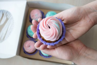 pembe ve mavi bir kutu cupcakes arka plan üzerinde bir kızın elinde krem ile Cupcake
