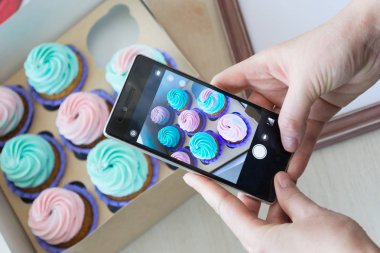 bir kutu kekler ve ahşap bir çerçeve ile bir telefon kadınların elleri tarafından fotoğraf çekimi