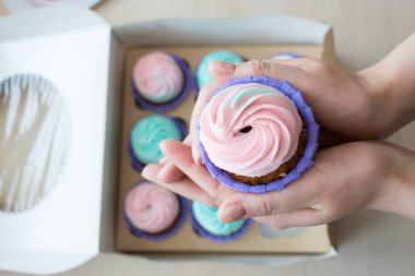 pembe ve mavi bir kutu cupcakes arka plan üzerinde bir kızın elinde krem ile Cupcake