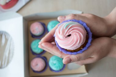 pembe ve mavi bir kutu cupcakes arka plan üzerinde bir kızın elinde krem ile Cupcake