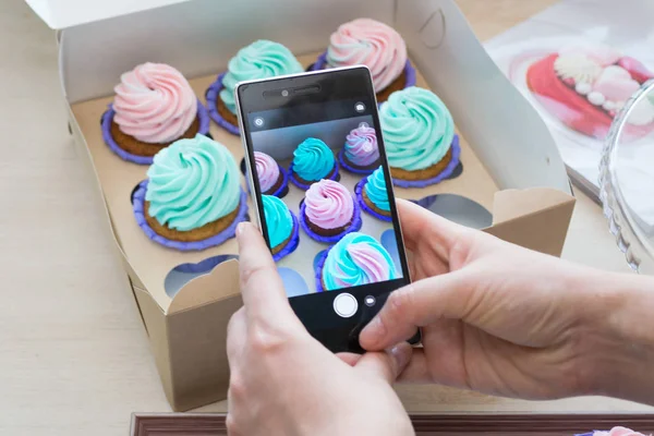 Kadınların elleri tarafından bir kutu bir telefon ile cupcakes ile fotoğraf çekimi