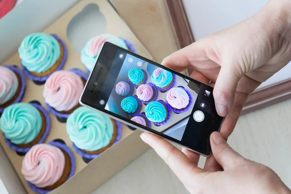 bir kutu kekler ve ahşap bir çerçeve ile bir telefon kadınların elleri tarafından fotoğraf çekimi