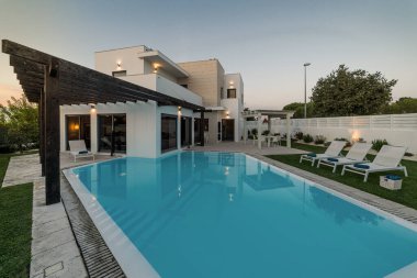 Bahçede yüzme havuzu ve ahşap pergulası olan modern bir ev.