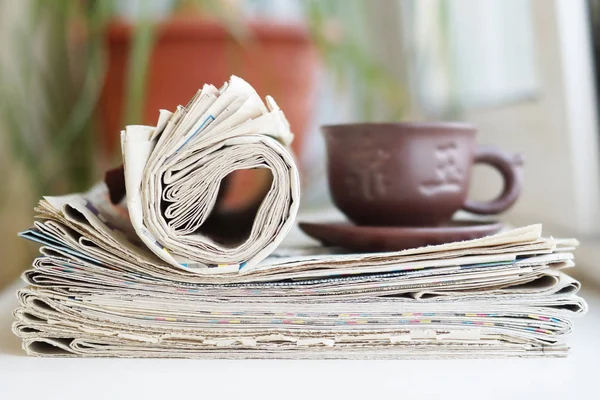 Stack of newspapers and cup of tea. Concept for business morning, reading fresh daily papers with news and having a breakfast. Journals and ceramic mug, selective focus on pages