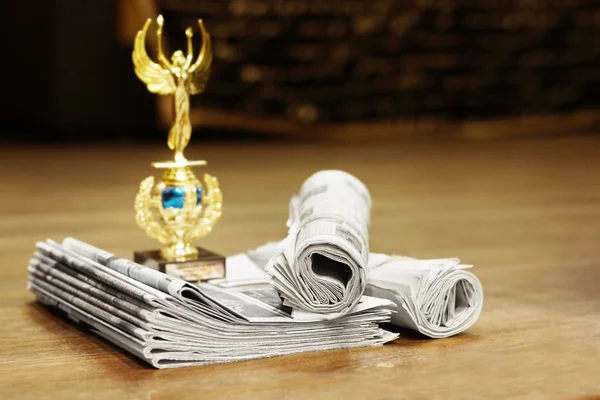 Newspapers and trophy. Daily papers with news stacked in a pile and golden prize on wooden table, selective focus
