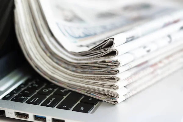 Newspapers and laptop. Folded papers with news stacked on computer. Information by different sources - paper pages of tabloid journals or on screen of electronic device