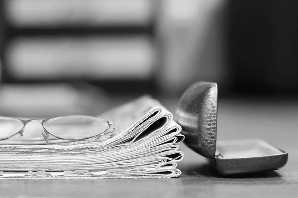 Newspapers. Stack of daily papers with news (tabloid journals) and reading glasses with open case on wooden table, side view