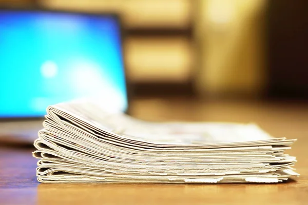Folded newspapers stacked in pile next to laptop. Computer and daily tabloid journals with news, side view