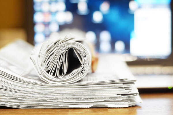 Складывал и катал газету на компьютере. Ежедневные газеты с новостями и открытым ноутбуком. Заголовки и статьи на бумажных страницах и экране с иконками на рабочем столе. Источники информации
    