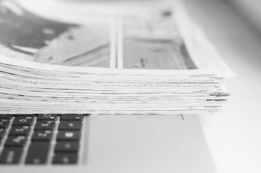 Gazete ve dizüstü bilgisayar. Bilgisayar haberleri ile günlük gazeteleri yığını. Sayfa başlıkları, makaleler ile katlanmış ve elektronik cihaz tuş takımında yığılmış. Modern araç ve eski dergiler, kağıt üzerinde odaklanmak 