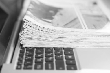 Gazete ve dizüstü bilgisayar. Bilgisayar haberleri ile günlük gazeteleri yığını. Sayfa başlıkları, makaleler ile katlanmış ve elektronik cihaz tuş takımında yığılmış. Modern araç ve eski dergiler, kağıt üzerinde odaklanmak 