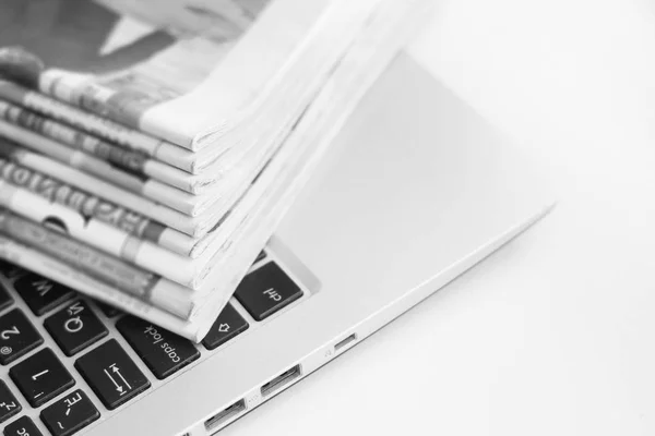 Newspapers and laptop. Pile of daily papers with news on the computer. Pages with headlines, articles folded and stacked on keypad of electronic device. Modern gadget and old journals, focus on paper