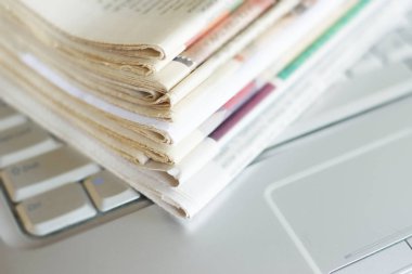 Gazete ve dizüstü bilgisayar. Bilgisayar haberleri ile günlük gazeteleri yığını. Sayfa başlıkları, makaleler ile katlanmış ve elektronik cihaz tuş takımında yığılmış. Modern araç ve eski dergiler, kağıt üzerinde odaklanmak 