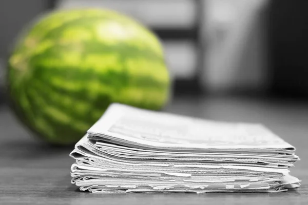 Newspapers and watermelon. Daily papers stacked in pile and fresh juicy fruit as concept for latest news and sensation. Tabloid journals pages with headlines and articles, selective focus on paper