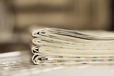 Gazete ve dizüstü bilgisayar. Bilgisayar haberleri ile günlük gazeteleri yığını. Sayfa başlıkları, makaleler ile katlanmış ve elektronik cihaz tuş takımında yığılmış. Modern araç ve eski dergiler, kağıt üzerinde odaklanmak 