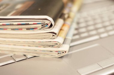Gazete ve dizüstü bilgisayar. Bilgisayar haberleri ile günlük gazeteleri yığını. Sayfa başlıkları, makaleler ile katlanmış ve elektronik cihaz tuş takımında yığılmış. Modern araç ve eski dergiler, kağıt üzerinde odaklanmak 