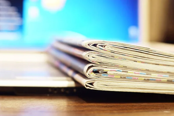 Newspapers and computer. Folded and rolled papers and magazines and open laptop. Concept for news by different sources of information - screen of electronic device or paper pages of tabloid