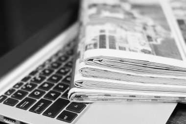 Gazete ve dizüstü bilgisayar. Bilgisayar haberleri ile günlük gazeteleri yığını. Sayfa başlıkları, makaleler ile katlanmış ve elektronik cihaz tuş takımında yığılmış. Modern araç ve eski dergiler, kağıt üzerinde odaklanmak 