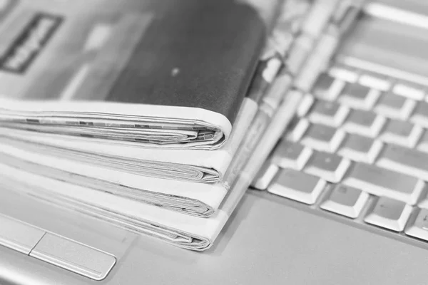 Newspapers and laptop. Pile of daily papers with news on the computer. Pages with headlines, articles folded and stacked on keypad of electronic device. Modern gadget and old journals, focus on paper