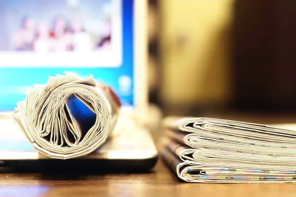 Newspapers and computer. Folded and rolled papers and magazines on keyboard of open laptop. Concept for news by different sources of information - screen of electronic device or paper pages of tabloid