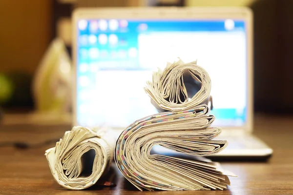 Fresh newspapers and open laptop. Papers with news on keyboard of personal computer with blurred screen on background. Different sources of information - digital and analog, internet or paper pages