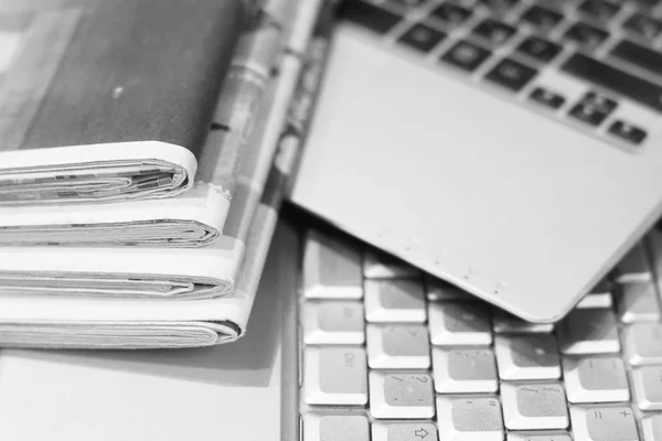 Business concept. Stack of newspapers and two computers. Work place of busy businessman with lots of sources of information - business papers with news and laptop connected to internet