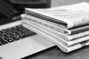 Gazete ve dizüstü bilgisayar. Bilgisayar haberleri ile günlük gazeteleri yığını. Sayfa başlıkları, makaleler ile katlanmış ve elektronik cihaz tuş takımında yığılmış. Modern araç ve eski dergiler, kağıt üzerinde odaklanmak
