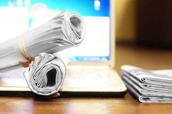 Newspapers and laptop. Pile of daily papers with news on the computer. Pages with headlines, articles folded and stacked on keypad of electronic device. Modern gadget and old journals, focus on paper