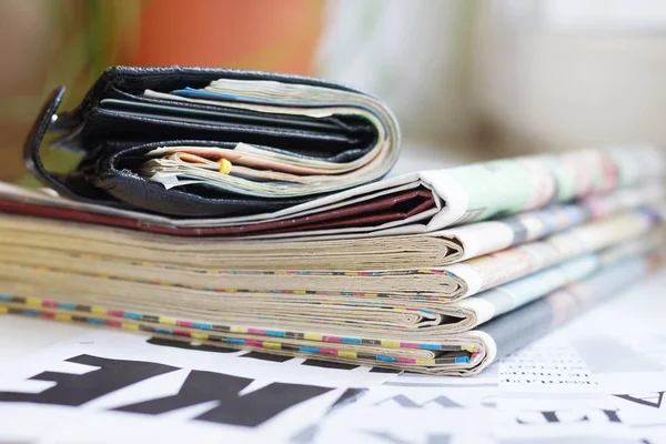 Business newspapers and magazines with latest news folded and stacked in pile and black leather wallet full of money, concept for successful business and finance management