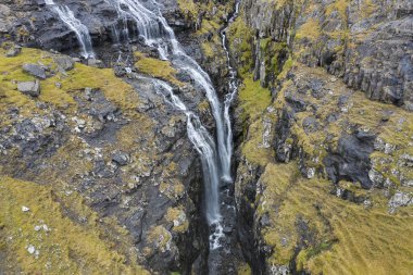 Şelaleler ve cascades bir kayalık ridge ve Faroe Adaları Streymoy Adası üzerinde Tjornuvik Köyü yakınındaki dar geçit boyunca havadan görünümü.