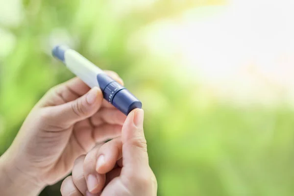 Primer plano de las manos de la mujer usando lanceta en el dedo para comprobar su sangre — Foto de Stock