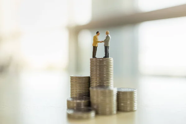 Business, Money and Work Concept. Two businessman miniature figures people standing and make hand shake on top of stack of coins.