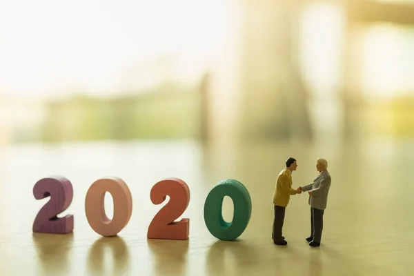 2020 İş ve Planlama Konsepti. İki işadamı minyatür figürü ayakta duruyor ve ahşap numaradan el sıkışıyor ve boşluğu kopyalıyor..