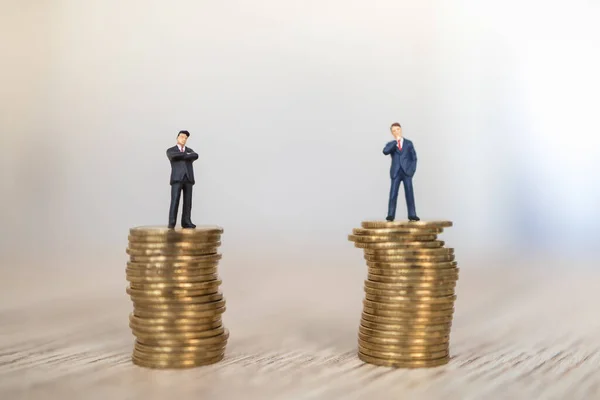 Business, Money Investment and Planning Concept.  Close up of two businessman miniature people figure standing on top of stack of gold coins on wooden table