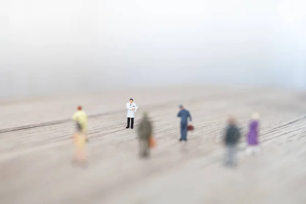 Healthcare Concept. Doctor miniature figure with patient clipboard with group of people with social distancing on wooden table and copy space