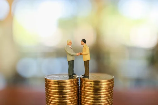 Business Money and Finance Concept, Two businessman miniature figure people standing and make a hand shake on top of stack of gold coin.