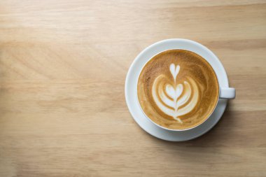 Beyaz kahve fincanının üst görüntüsü sütlü sanat köpüğü kalp şeklinde ahşap masa ve fotokopi alanı..