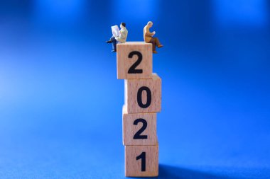 2021 İş ve Haber Konsepti. İki minyatür işadamı oturuyor, gazete okuyor ve mavi arka planda tahta bloklar üzerine kitap okuyor..