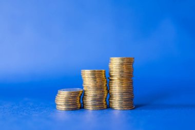 Para, İş ve Tasarruf Konsepti. Mavi arkaplandaki üç yığın altın madeni paranın fotokopi alanı ile yakınlaştırılması.