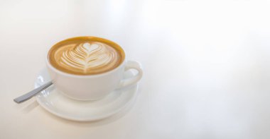 Süt köpüklü sütlü sütlü kahve fincanı tabakta resim ve fotokopi alanı ile beyaz masada kaşık şeklinde kahve..