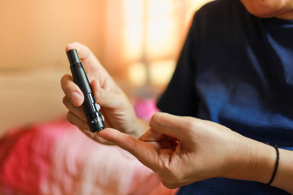 Close up of man hands using lancet on finger to check blood sugar level by Glucose meter. Use as Medicine, diabetes, glycemia, health care and people concept.