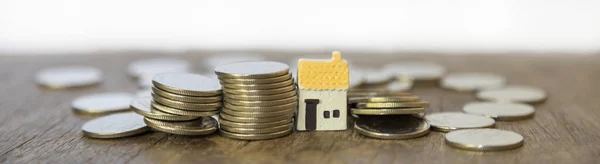 Business, Mortgage, Home Loan Cover Page Concept. Closeup of three mini house toy with stack and pile of coins on wooden table.