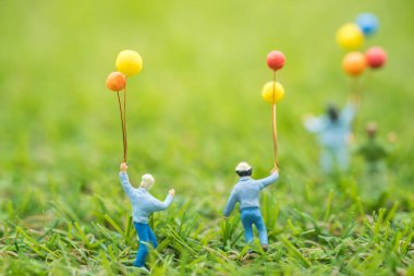 Çocukluk ve aile kavramı. Bir grup çocuk minyatür figürlere yakın çekim. İnsanlar yeşil çimlerin üzerinde koşup balonla oynuyorlar..