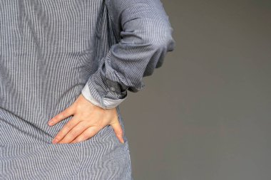 Gri bir arka plan üzerinde izole böbrek ağrısı olan bir genç kadın görmek. Genç kadın elini Sırtının alt clasping sırt ağrısı ile. Lastik ağrısı, bel ağrısı acı kadın.