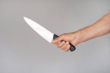 Hand of a man holding a knife isolated on a gray background . Big kitchen knife in man hand. clipart