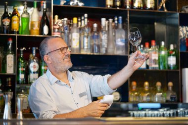 Barmen cam temizler. Yakışıklı bir barmen bir bardak şarap bardakları parlatıyor. Hizmet kavramı.