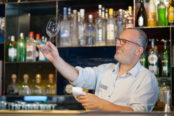 Barmen cam temizler. Yakışıklı bir barmen bir bardak şarap bardakları parlatıyor. Hizmet kavramı.